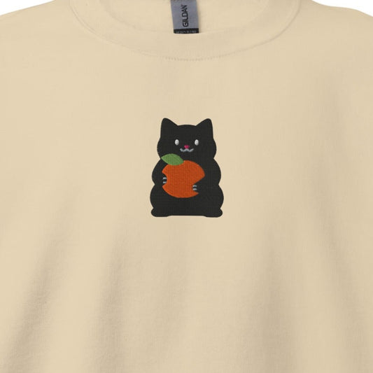 Close-up of the Mikan Cat embroidery on a sand crewneck sweatshirt: a chubby black cat hugging a mandarin orange